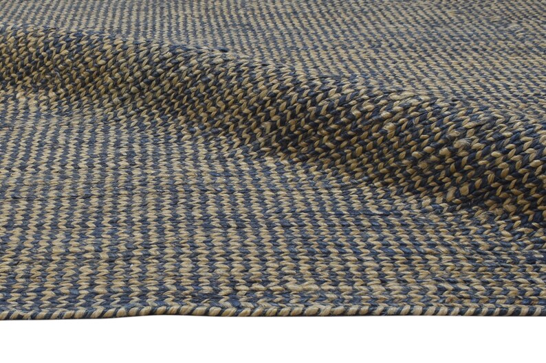 Puede incluir: Primer plano de una alfombra tejida con un patr&oacute;n repetitivo de rayas verticales azules y beige alternas. La alfombra tiene una superficie texturizada y un borde enrollado, lo que sugiere un material de fibra natural.