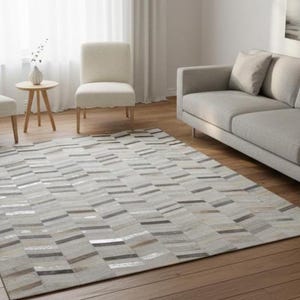 May include: A rectangular area rug with a geometric pattern in shades of gray, beige, and brown. The rug is placed on a hardwood floor in a living room setting. Two cream-colored chairs and a gray sofa are also visible.