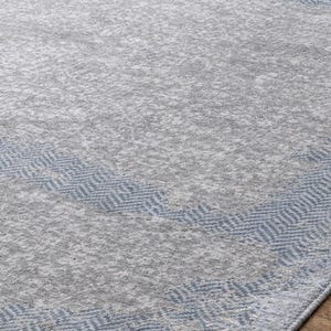 May include: A gray area rug with a blue geometric border. The rug has a textured appearance and a subtle pattern throughout the gray field. The blue border features a repeating chevron design, adding visual interest to the rug's edge.