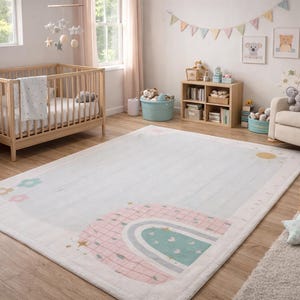 May include: A nursery room featuring a light-coloured wooden cot, chest of drawers, and a beige rocking chair. A large white rug with a rainbow and sun design is on the floor. The room is decorated with soft colours and children's artwork.