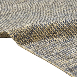 Puede incluir: Primer plano de una alfombra tejida con superficie texturizada. La alfombra presenta un patr&oacute;n de fibras azules y beige alternas, creando un sutil efecto de rayas. El borde de la alfombra es visible, mostrando la construcci&oacute;n tejida.