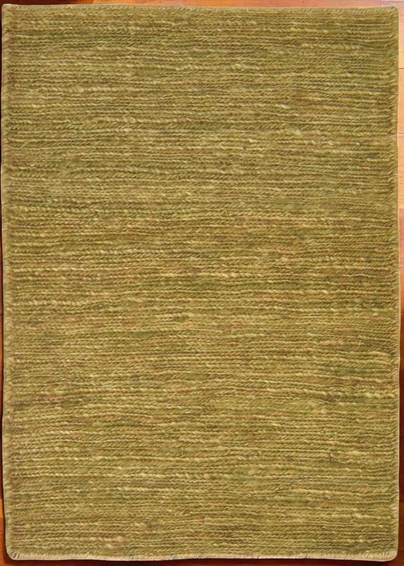 May include: A rectangular rug with a textured, woven appearance. The rug is primarily olive green with lighter, natural-toned fibers interspersed throughout. The weave pattern creates a subtle horizontal striped effect. The rug's edges are neatly finished.