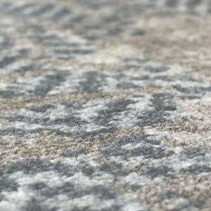 May include: Close-up of a textured rug with a repeating pattern. The rug features a mix of gray, white, and brown tones, creating a neutral and versatile design. The fibers appear soft and plush, suggesting comfort.