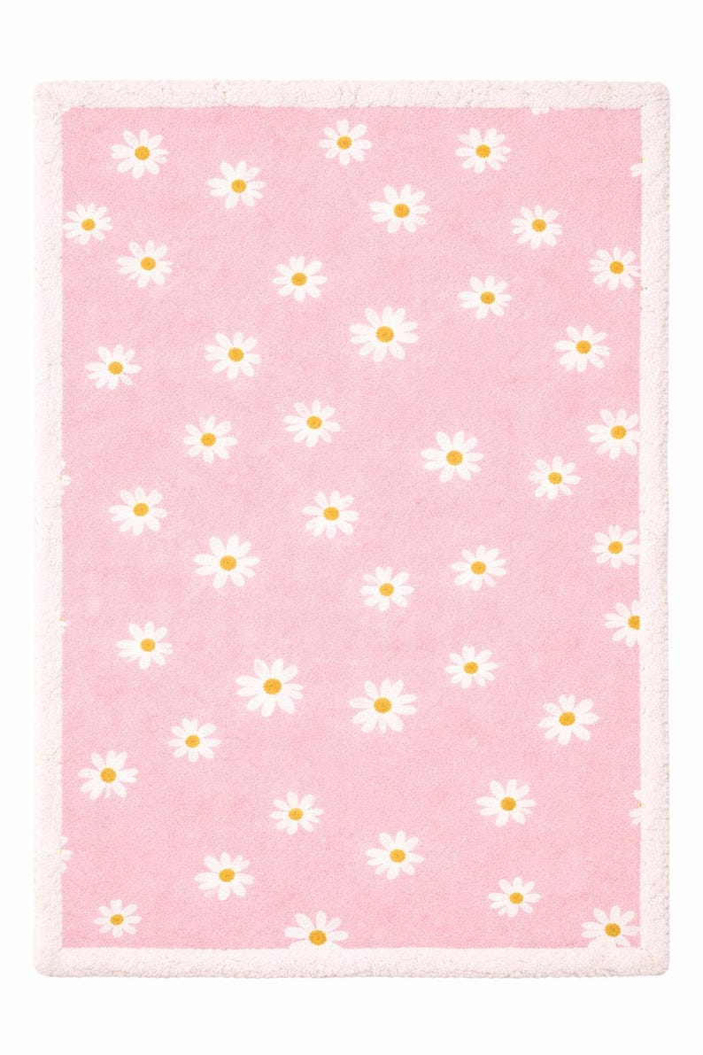 May include: A rectangular pink rug featuring a repeating pattern of white daisies with yellow centres. The rug has a white border. The design is simple and cheerful, suitable for a bedroom or nursery.