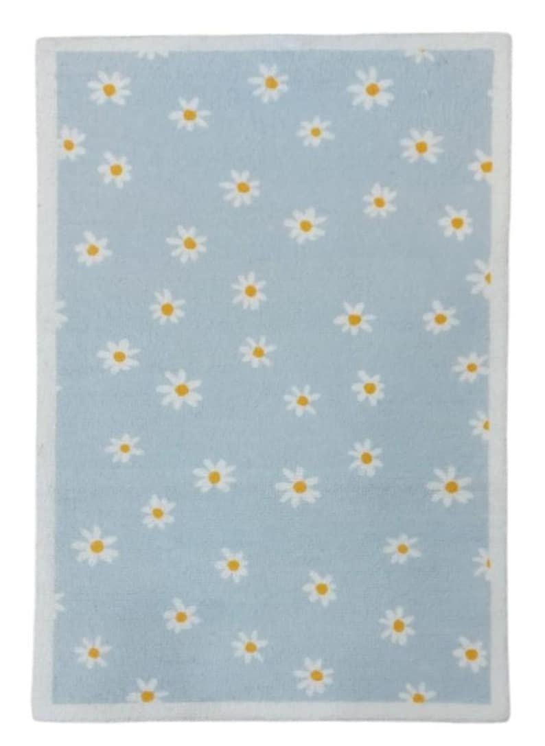 May include: A rectangular, pale blue rug with a white border. The rug features a pattern of white daisies with yellow centres. The daisies are evenly spaced, creating a cheerful design. The rug's dimensions are in centimetres.