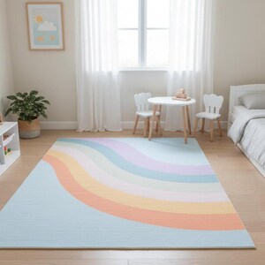 May include: A pastel rainbow rug in a child's bedroom. The rug features a light blue base with curved stripes of pink, purple, yellow, and orange. The room also includes a white bed, table, chairs, and a bookshelf.