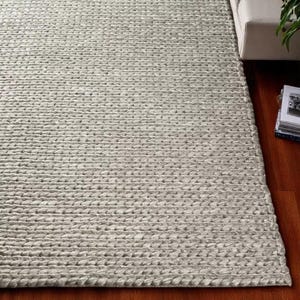 May include: A large, rectangular, light gray rug with a textured, braided appearance. The rug is made of a thick, durable material and has a neutral color that would complement various interior design styles. The rug is placed on a dark wood floor.