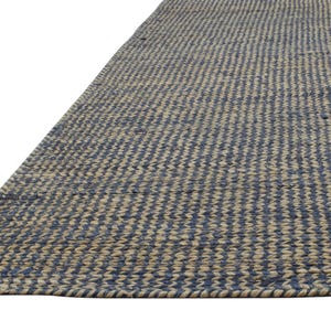 Puede incluir: Una alfombra rectangular con un patr&oacute;n tejido de rayas azules y beige alternas. La alfombra est&aacute; hecha de fibras naturales y tiene un aspecto texturizado. El borde de la alfombra es visible, mostrando un borde tejido apretado.