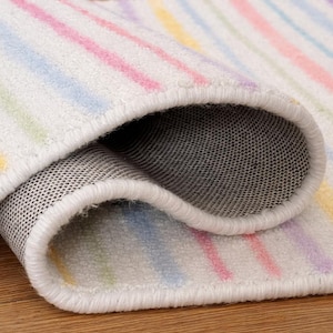 May include: Rolled-up rug with pastel stripes in pink, yellow, blue, and purple on a white background. The rug has a white border and a grey, textured underside. The rug is on a wooden surface. The rug's measurements are in centimeters.