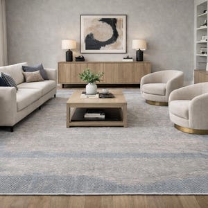 May include: A modern living room featuring a light-colored sofa with accent pillows, two swivel chairs, and a wooden coffee table. The room has a large area rug with a blue border and a neutral color palette. Two lamps sit on a wooden console.