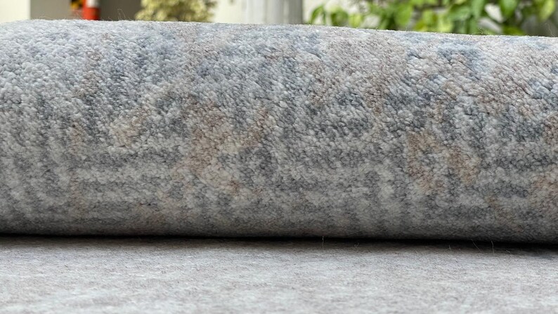 May include: Rolled-up area rug with a textured surface. The rug features a pattern of gray, blue, and beige hues. The fibers create a soft, plush appearance, suitable for home decor.