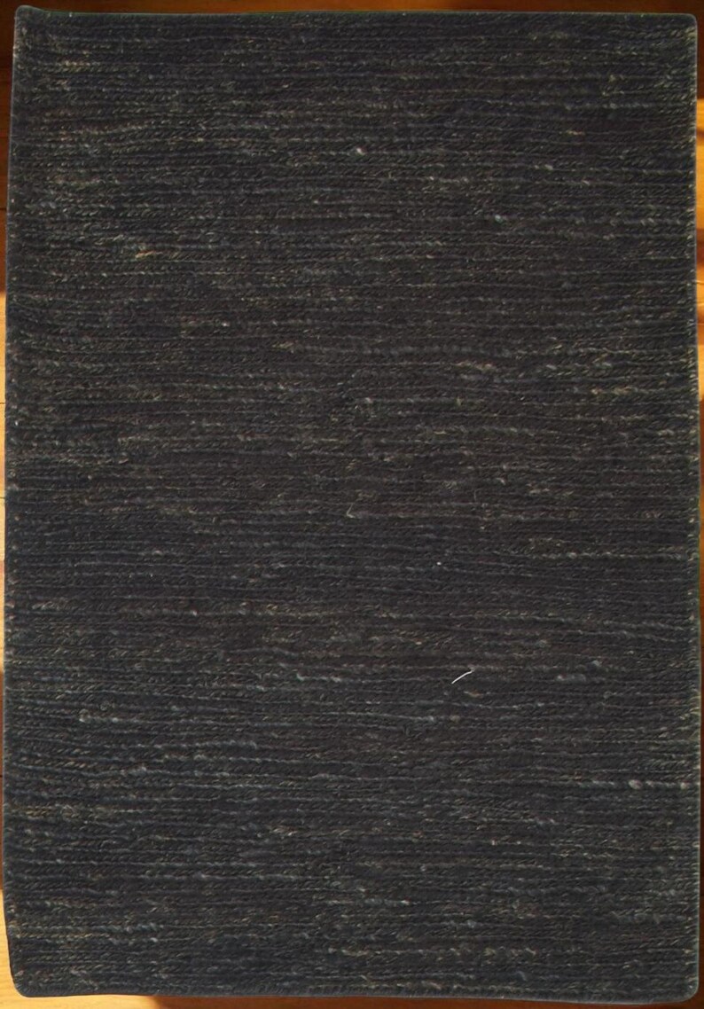 May include: A rectangular, dark charcoal-colored rug with a textured surface. The rug's fibers create a subtle, horizontal pattern. The rug is likely made of natural fibers, suitable for home decor.