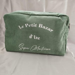 Pu&ograve; includere: Un beauty case rettangolare in velluto a coste verde salvia. La borsa presenta il testo "Le Petit Bazar d'Une Super Ma&icirc;tresse" in scrittura bianca. La borsa ha una chiusura con cerniera e una texture a coste.