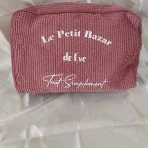 Pu&ograve; includere: Un beauty case in velluto a coste rosa antico con la scritta "Le Petit Bazar de Eve Tout Simplement" in corsivo bianco. La borsa rettangolare ha una trama a coste e una chiusura con cerniera.