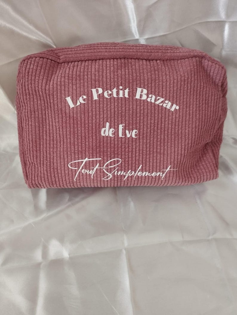 Pu&ograve; includere: Un beauty case in velluto a coste rosa antico con la scritta "Le Petit Bazar de Eve Tout Simplement" in corsivo bianco. La borsa rettangolare ha una trama a coste e una chiusura con cerniera.