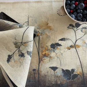 May include: A beige linen table runner with a watercolor floral design in shades of blue, brown, and yellow. The runner features a repeating pattern of stylized flowers and leaves.