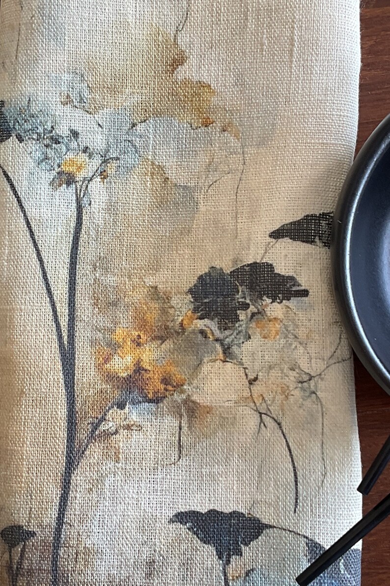 May include: A beige linen fabric with a floral design printed on it. The design features black silhouettes of birds and brown and white watercolor flowers.