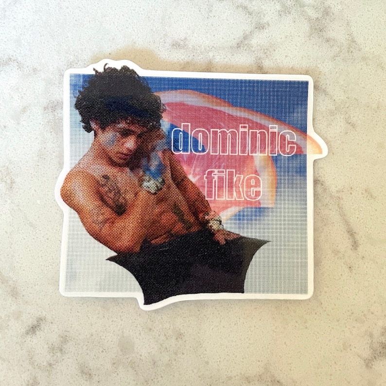 Puede incluir: Una pegatina con una foto de Dominic Fike, cantante y compositor, con el texto "dominic fike" en letras blancas sobre un fondo azul y rojo.