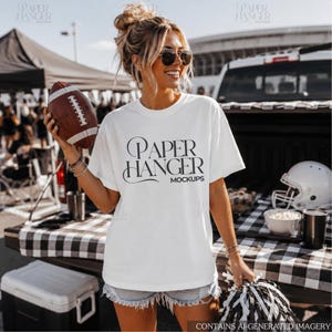 May include: A white short-sleeved t-shirt featuring the black text Paper Hanger Mockups printed on the front. The shirt has a crew neckline and a relaxed fit, showcasing a bold graphic design with stylized lettering across the chest area.
