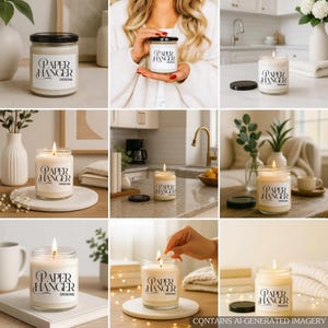 May include: Glass jar candle with a black lid. The candle has a white label with the text "PAPER HANGER DESIGNS" in a black, elegant font. The candle is lit, and the flame is visible. The candle is on a white surface.