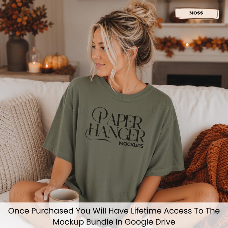 Pode incluir: Uma t-shirt de manga curta verde-musgo com o texto preto "PAPER HANGER MOCKUPS" estampado na frente. A pe&ccedil;a tem gola redonda e um corte descontra&iacute;do. O texto est&aacute; escrito numa fonte serifada estilizada com elementos decorativos.