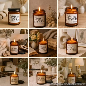 May include: A collection of lit candles in amber-colored glass jars with black lids. Each jar has a white label with the text "PAPER HANGER DESIGNS". The candles are placed on various surfaces with decorative elements, creating a warm and inviting ambiance.
