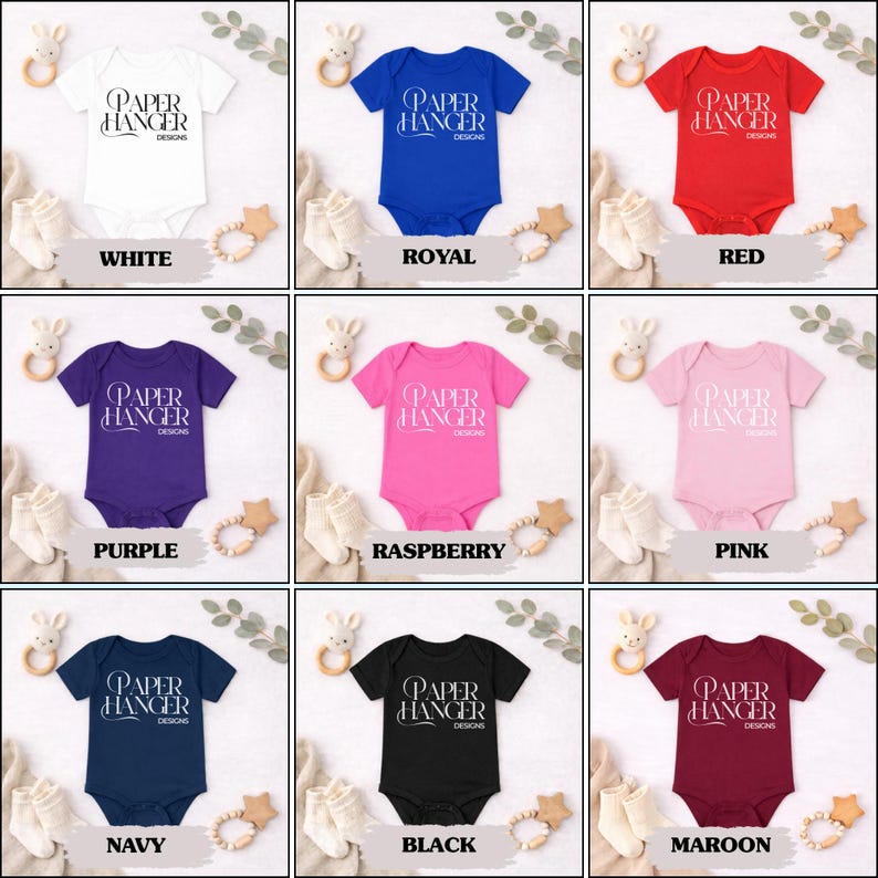 Puede incluir: Una colecci&oacute;n de bodies para beb&eacute;s en varios colores: blanco, azul real, rojo, morado, frambuesa, rosa, azul marino, negro y granate. Cada body presenta el texto "PAPER HANGER DESIGNS".