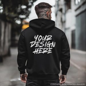 May include: Black hoodie with the text "YOUR DESIGN HERE" in white. The hoodie is being worn by a person with tattoos on their neck and arm. The image is taken from behind, with a blurred background.