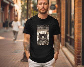 May include: A black t-shirt with a graphic of a pilot wearing a helmet and goggles. The text on the shirt reads "I'm almost a pilot I'm almost a pilot I'm almost a pilot".