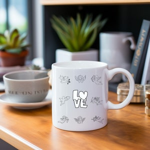 May include: White ceramic mug with a black and white design of cupids and the word "LOVE" with a heart.