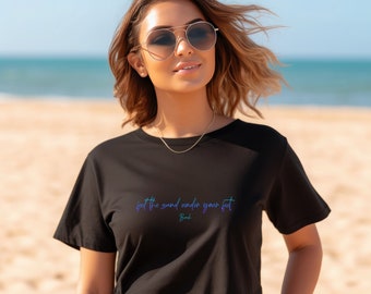 May include: A black cropped t-shirt with the text "feel the sand under your feet" in a blue and purple gradient. The text "Beach" is written below in a smaller font.