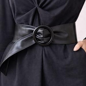 Peut inclure: Robe noire avec une large ceinture noire à boucle ronde. La ceinture souligne la taille, créant une silhouette définie. La robe a des manches longues et un col en V. Le tissu est doux.
