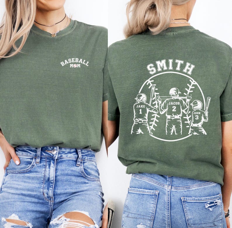 Puede incluir: Camiseta verde con el texto "Baseball Mom" en la parte delantera y un dise&ntilde;o de tem&aacute;tica de b&eacute;isbol en la parte posterior. El dise&ntilde;o presenta a tres jugadores de b&eacute;isbol con sus nombres y n&uacute;meros: Jake 1, Jacob 2 y John 3. El texto "Smith" est&aacute; por encima del dise&ntilde;o.