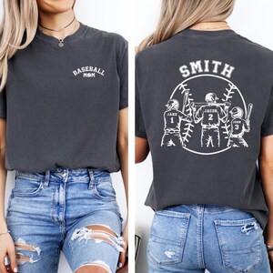 Puede incluir: Una camiseta gris oscuro con el texto "Baseball Mom" en la parte delantera y un dise&ntilde;o de b&eacute;isbol con el texto "Smith" y los nombres "Jake", "Jacob" y "John" en la parte posterior.