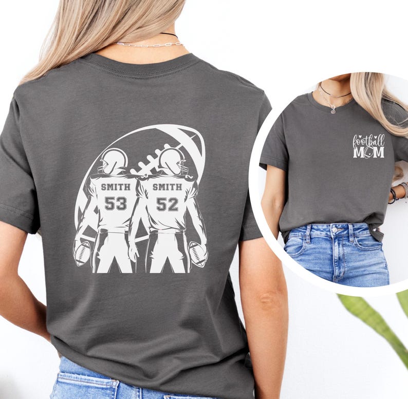 May include: Gray t-shirt featuring a football-themed graphic. The back of the shirt displays two football players with the name "Smith" and numbers 53 and 52. The front of the shirt has the text "football MOM".