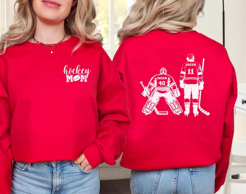 May include: Red sweatshirt with the text "hockey mom" and a hockey puck on the front. The back of the sweatshirt has a white silhouette of two hockey players, one is a goalie and the other is a forward.
