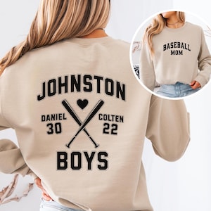 May include: Beige sweatshirt with the word "JOHNSTON" arched across the back in black, with crossed baseball bats and a heart. Below are the names "DANIEL 30" and "COLTEN 22" and the word "BOYS". A smaller image shows a beige sweatshirt with "BASEBALL MOM" in black.