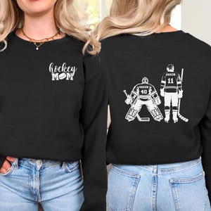 May include: Two black long-sleeved shirts with a hockey theme. One shirt says "hockey mom" with a hockey puck. The other shirt has two hockey players, one with the number 40 and the other with the number 11.