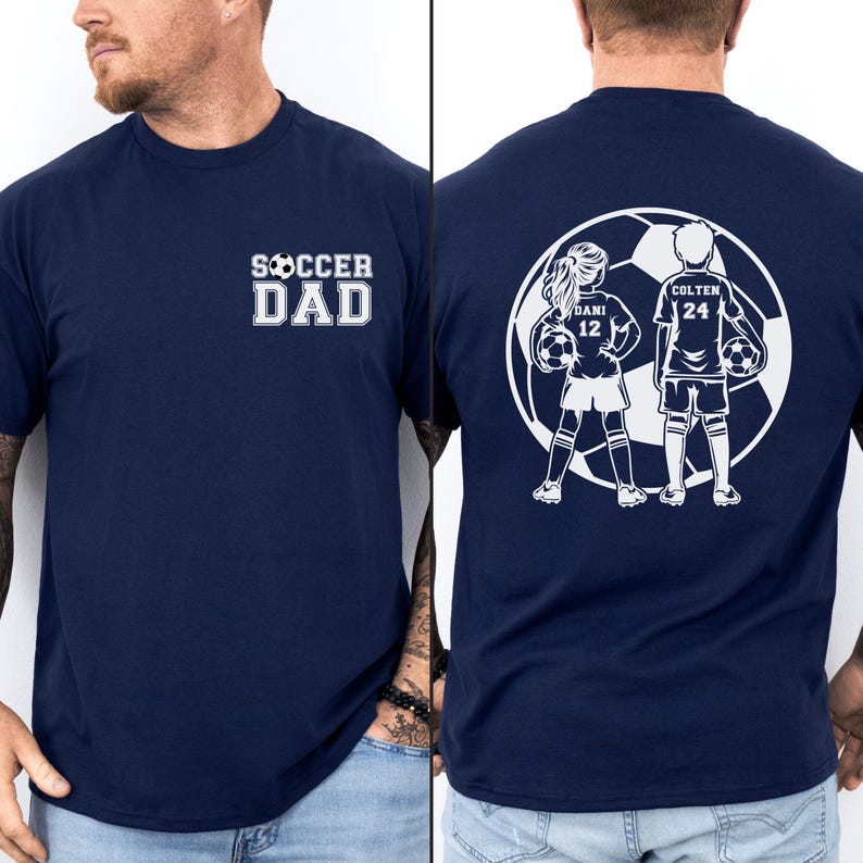 May include: Navy blue t-shirt with the text "SOCCER DAD" in white on the front. The back features a white graphic of two soccer players inside a soccer ball, with the names "DANI 12" and "COLTEN 24".