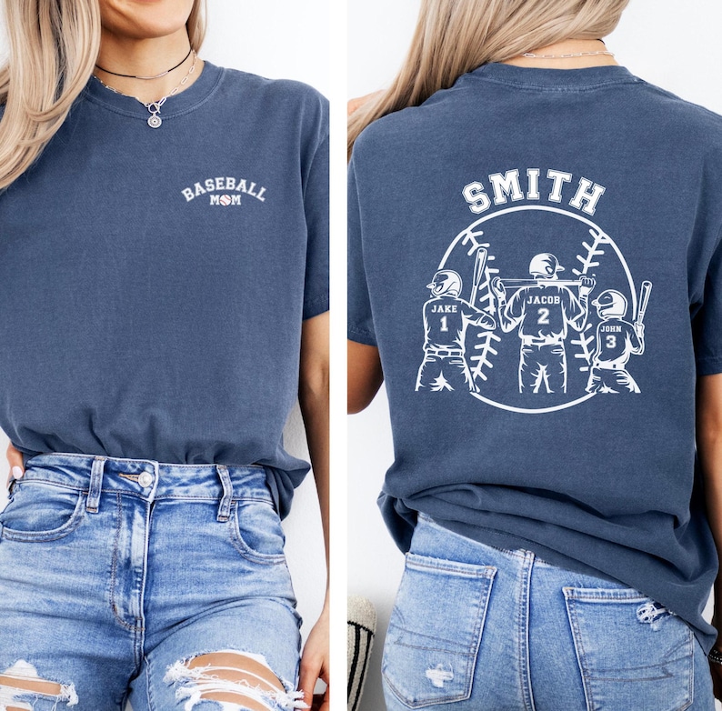 Puede incluir: Una camiseta azul marino con el texto "Baseball Mom" en la parte delantera y un dise&ntilde;o de tem&aacute;tica de b&eacute;isbol en la parte posterior. El dise&ntilde;o de la parte posterior presenta a tres jugadores de b&eacute;isbol con los nombres "Jake", "Jacob" y "John" y sus n&uacute;meros correspondientes 1, 2 y 3. El texto "Smith" est&aacute; por encima del dise&ntilde;o.