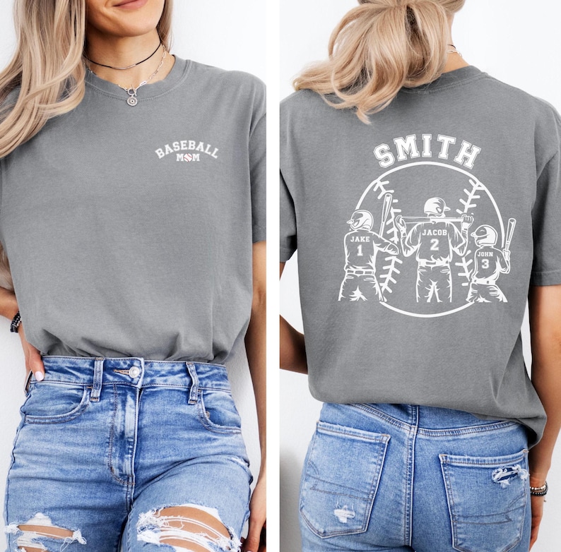 Puede incluir: Camiseta gris con un dise&ntilde;o de b&eacute;isbol blanco y el texto "Baseball MSM" en la parte delantera. La parte posterior de la camiseta tiene un dise&ntilde;o de b&eacute;isbol blanco con el texto "Smith" y tres jugadores de b&eacute;isbol con los nombres "Jake", "Jacob" y "John" en sus camisetas.