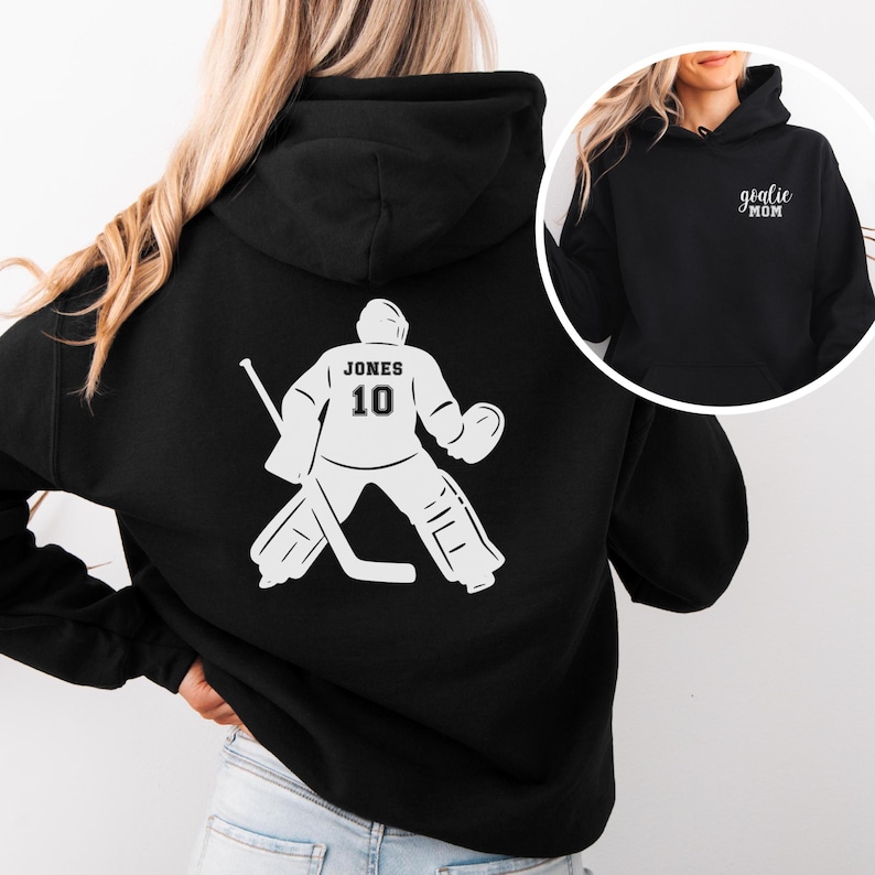 Op de afbeelding: Zwarte hoodie met een witte hockey goalie afbeelding op de rug met de naam "JONES" en het nummer "10". Een kleinere afbeelding toont een zwarte hoodie met de tekst "goalie mom".