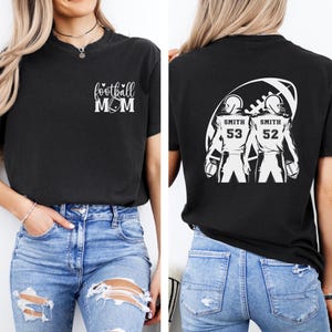 May include: Black t-shirt with "football MOM" text and a football graphic on the front. The back of the shirt features two football players with the name "Smith" and numbers 53 and 52. The shirt is made of a soft material.