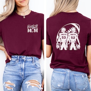 May include: Burgundy t-shirt with the text "football MOM" and a football graphic. The back of the shirt features a football design with two football players, the name "Smith", and the numbers 53 and 52.