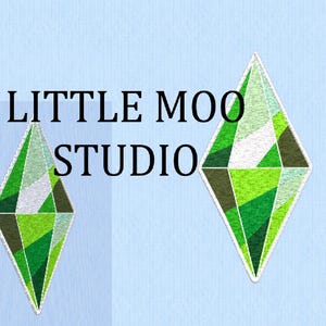 Puede incluir: Dos parches en forma de diamante con diseños geométricos verdes, blancos y marrones sobre un fondo azul claro. El texto "LITTLE MOO STUDIO" está encima de los parches.