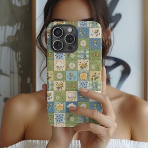 May include: A smartphone case featuring a patchwork grid design in shades of green, blue, and cream. The pattern includes repeating illustrations of daisies, yellow stars, butterflies, rain clouds, and small blue creatures on checkered backgrounds.