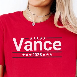 May include: Red t-shirt with white text that says "Vance 2028" with stars above and below the text.