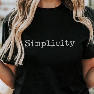 Puede incluir: Una camiseta negra con la palabra "Simplicity" impresa en blanco en la parte delantera.