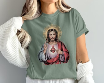 Könnte beinhalten: Salbeigrünes T-Shirt mit einem religiösen Aufdruck. Die Grafik zeigt eine Figur mit Heiligenschein, langem Haar und Bart, die rote und weiße Gewänder trägt. Ein flammendes Herz ist auf der Brust der Figur zu sehen. Die Figur hebt eine Hand zum Segen.