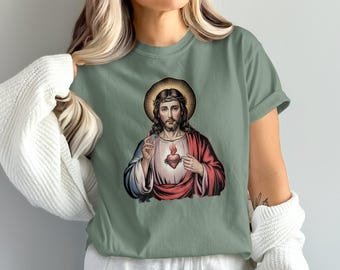 Könnte beinhalten: Salbeigrünes T-Shirt mit einer religiösen Illustration. Die Grafik zeigt eine Figur mit Heiligenschein, langem Haar und Bart, mit einem flammenden Herzen auf der Brust. Die Figur trägt ein rotes und weißes Gewand.